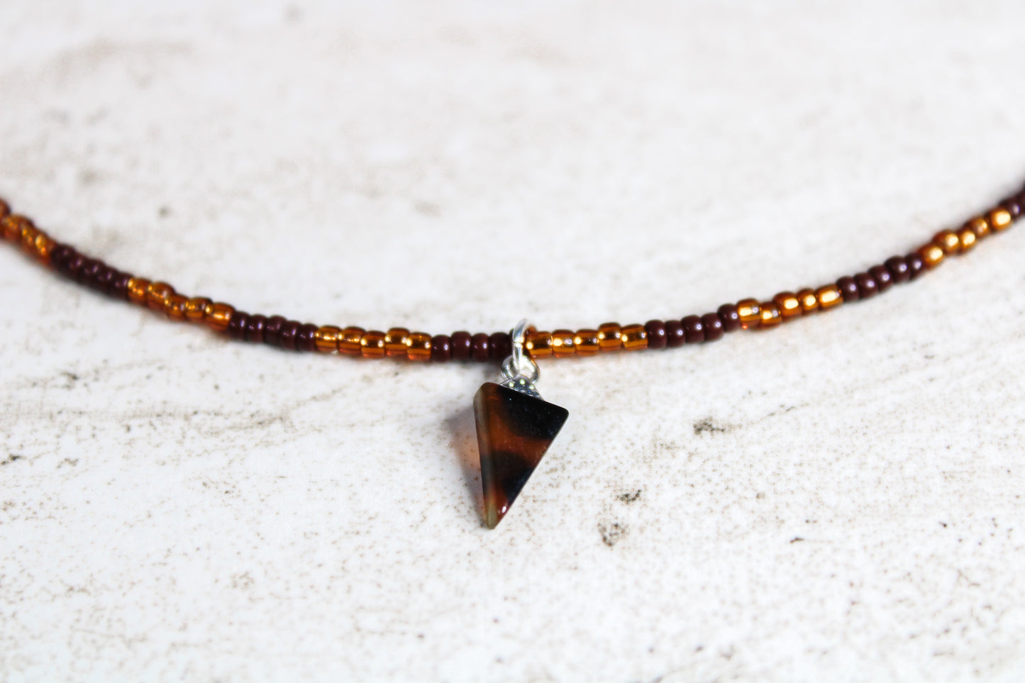 Close-up of the brown and copper seed beads and triangle tortoiseshell charm, showing the subtle shimmer and color variation.