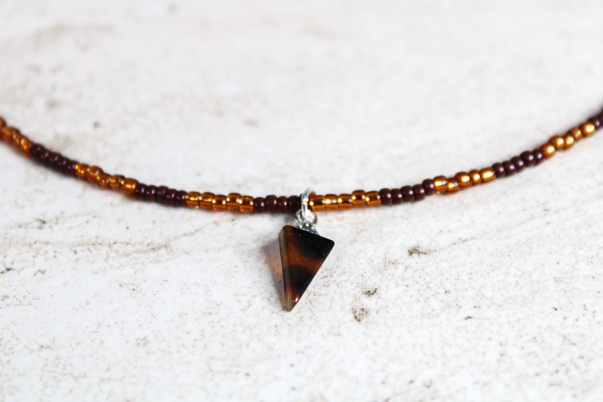 Close-up of the brown and copper seed beads and triangle tortoiseshell charm, showing the subtle shimmer and color variation.